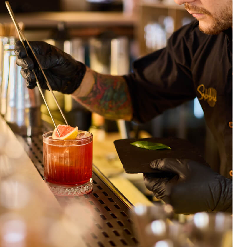 Bartender decorando un cóctel rojo con pomelo en la barra de Sabbia