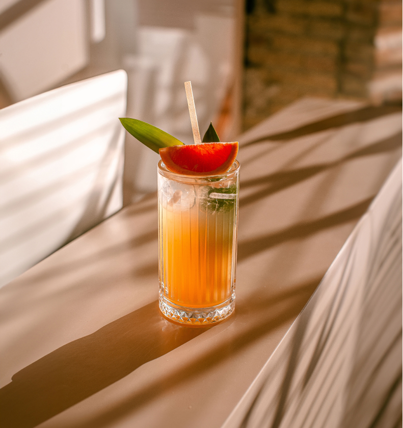 Cóctel naranja con pomelo en vaso tallado sobre la barra iluminada por el sol