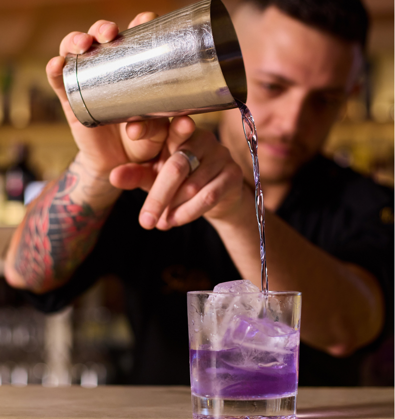 Bartender sirviendo un cóctel morado sobre hielo en la barra de Sabbia