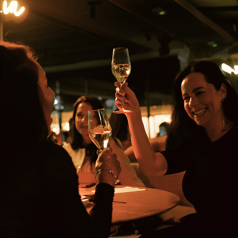Amigas brindando con vino blanco en una mesa de Sabbia por la noche