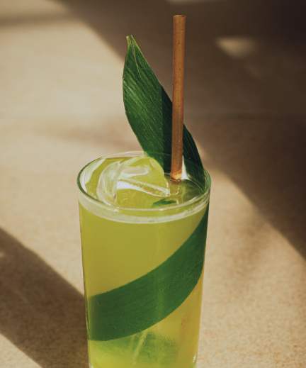 Cóctel verde en vaso alto decorado con hoja de palma y pajita de bambú