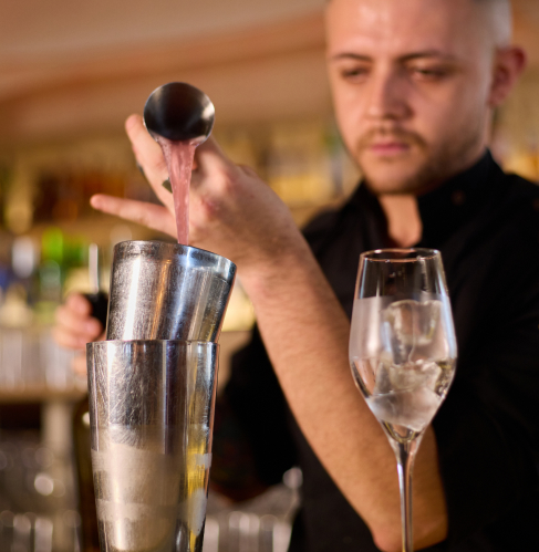 Bartender de Sabbia preparando un cóctel con coctelera y medidor en la barra